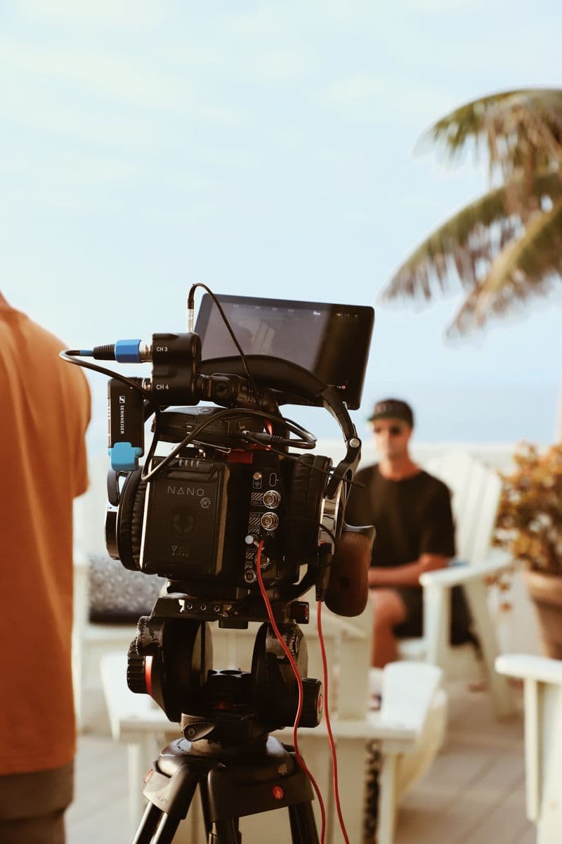 A cinema camera on a tripod, set up on a terrace above the beach