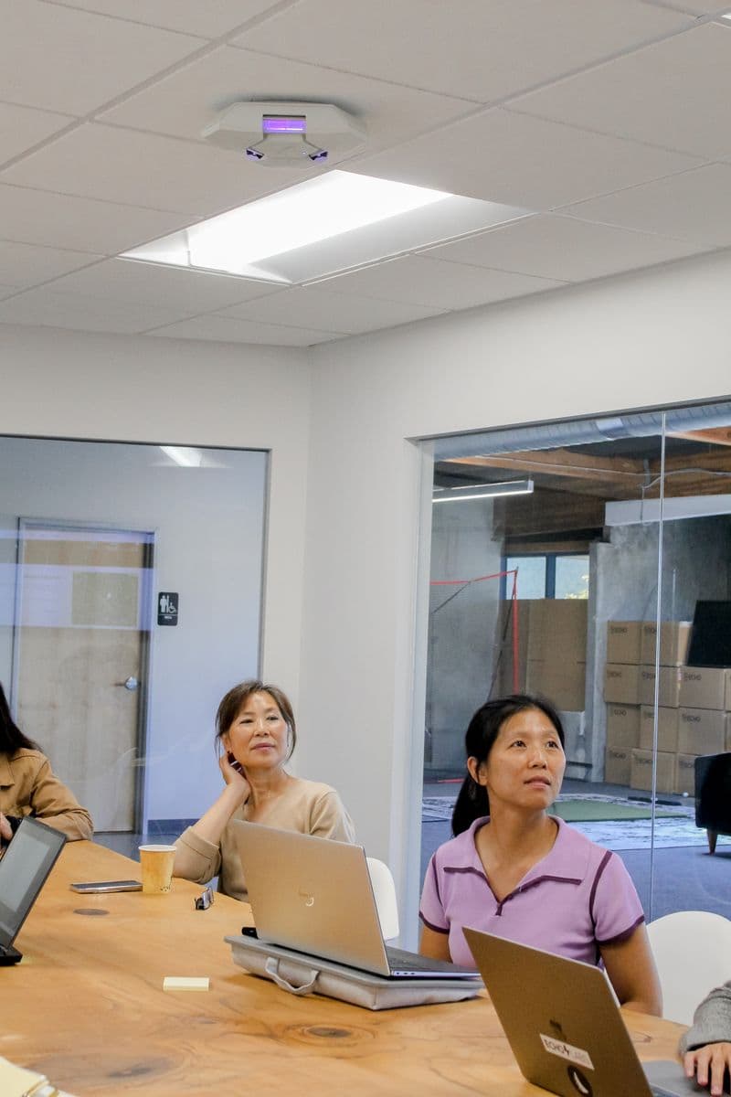 Two colleagues at a meeting table looking up at a Lumenizer unit