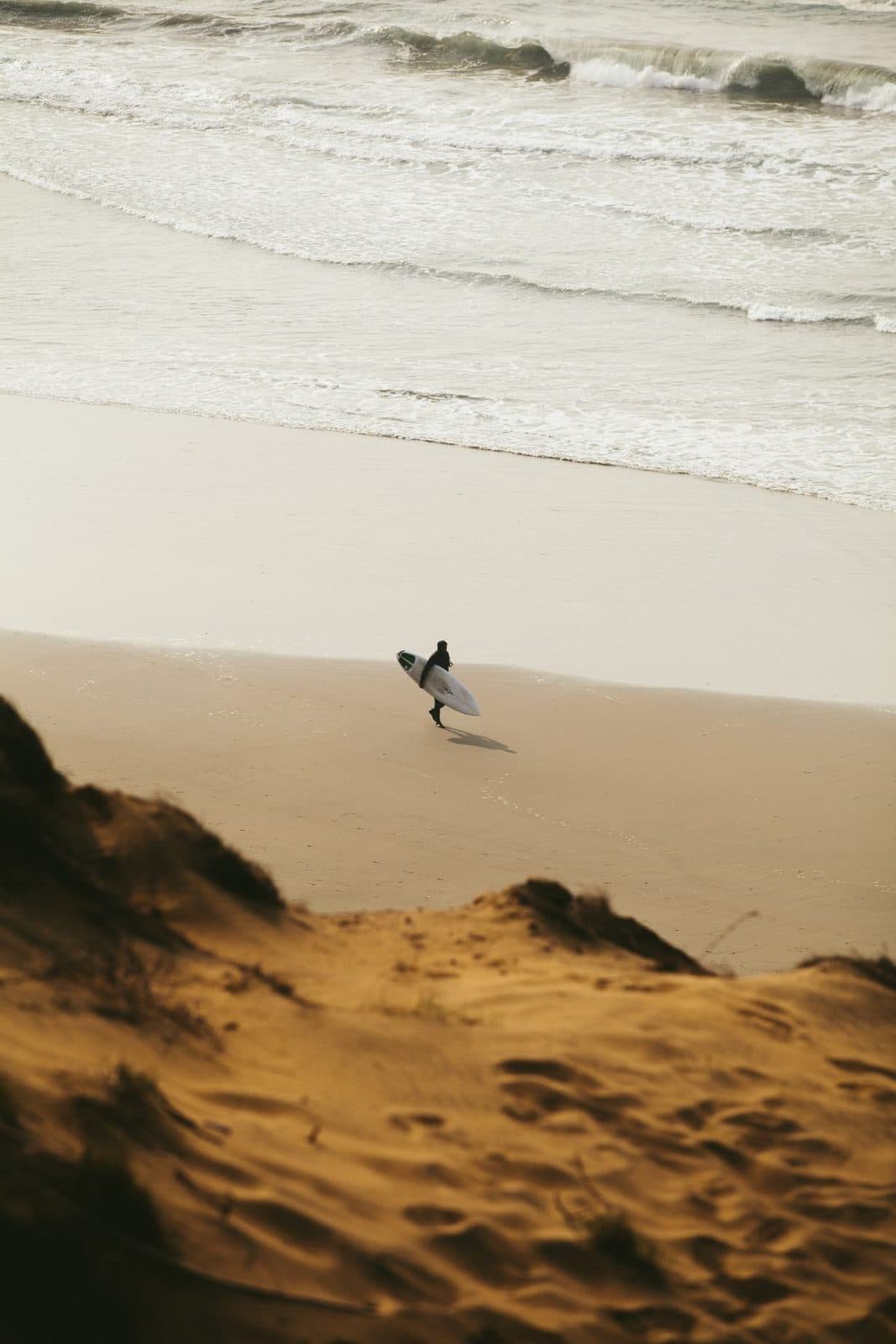 A surfer walking a dune path to the beach